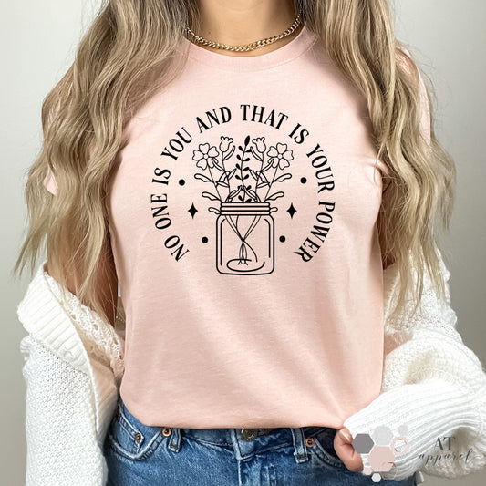 Woman wearing No One Is You Tee in heather peach with black print